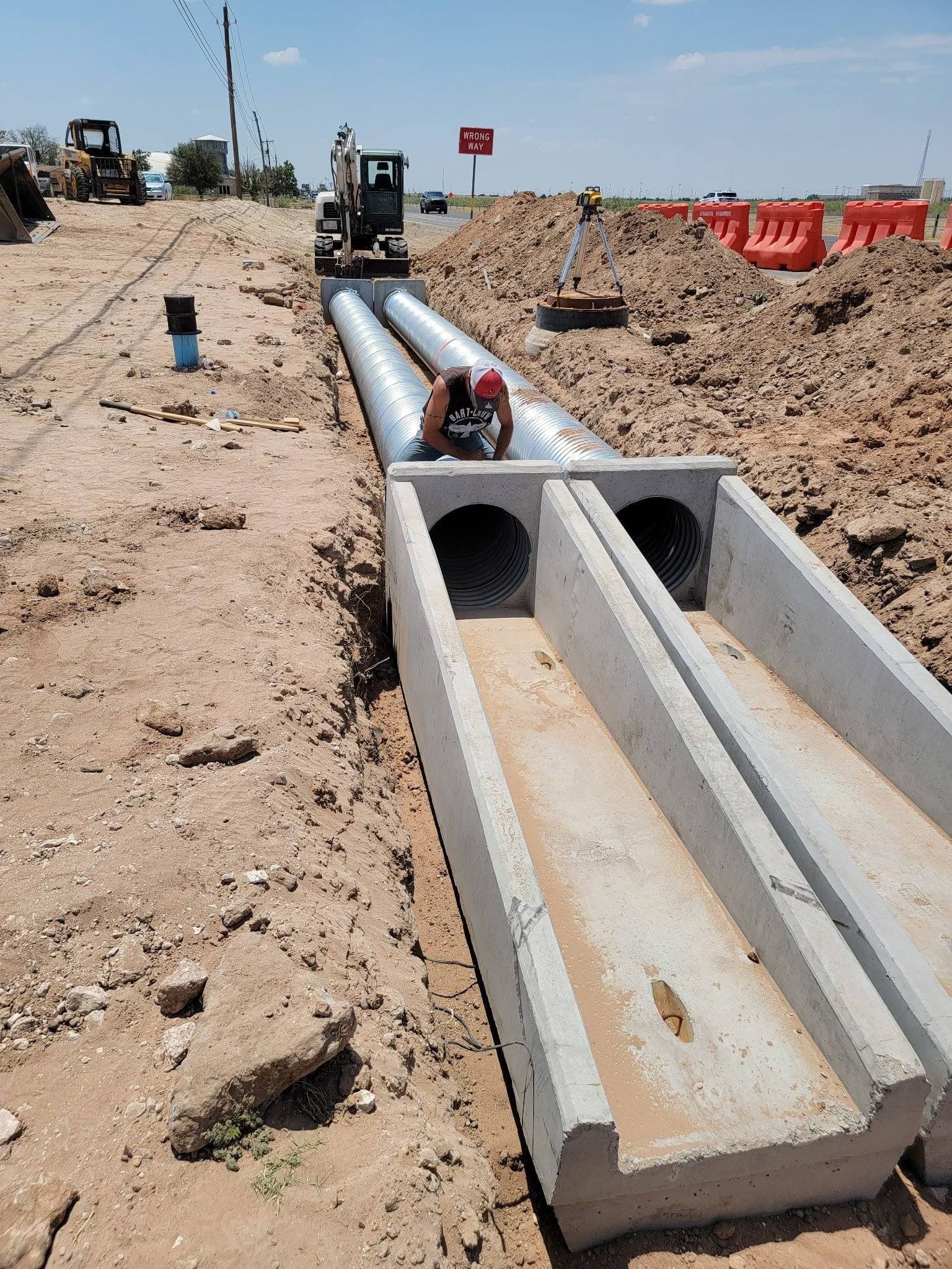 Excavator placing a concrete culvert in a trench