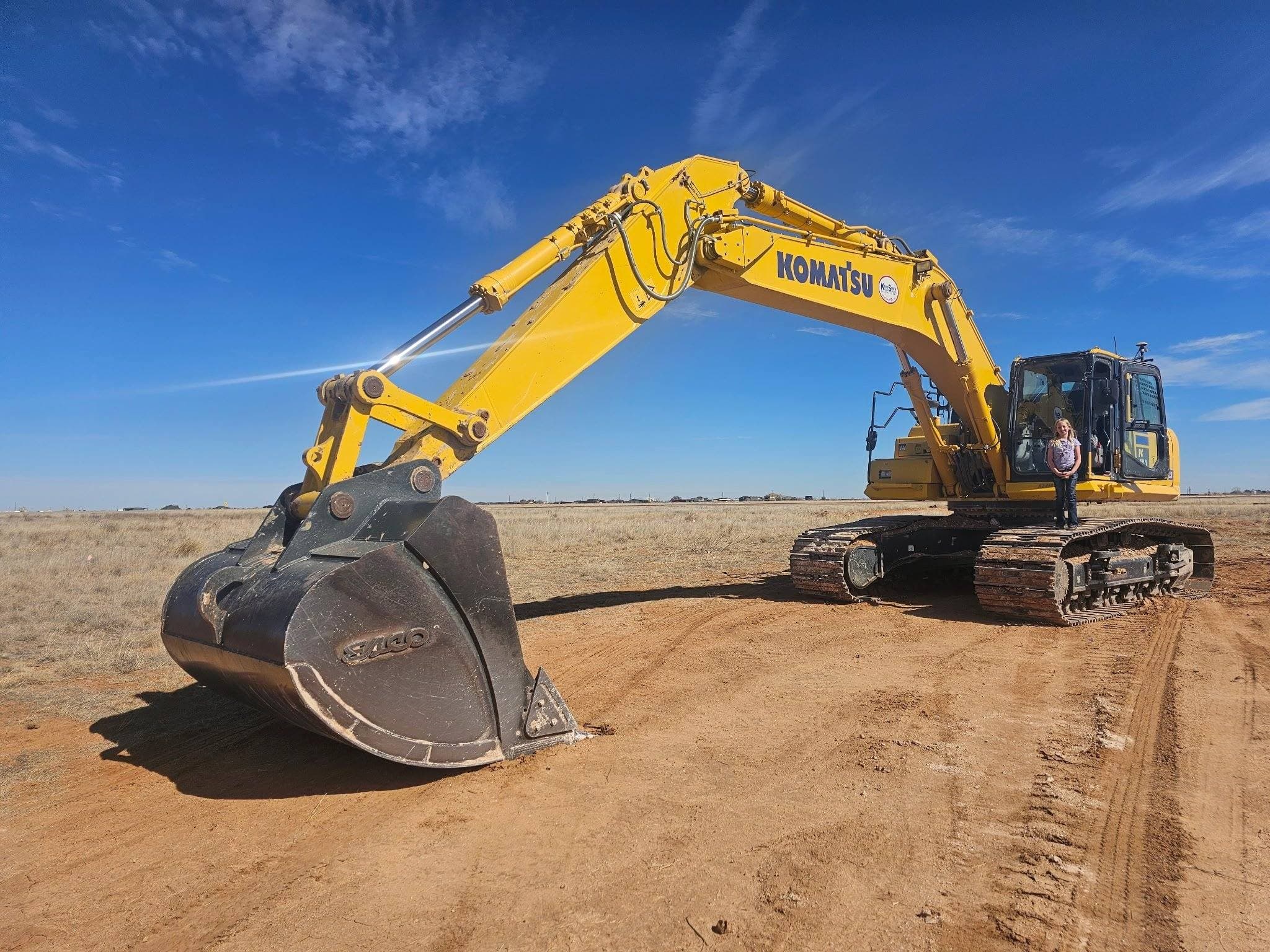 Rangefinder Excavation crew member standing on a large excavator on a West Texas job site