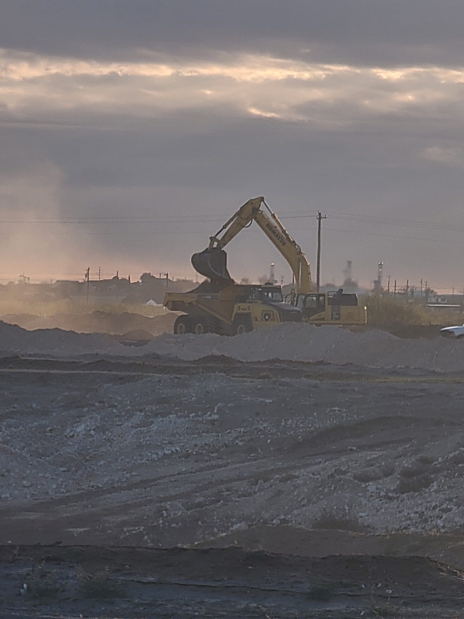 Excavator and haul truck moving earth on a West Texas job site at dusk